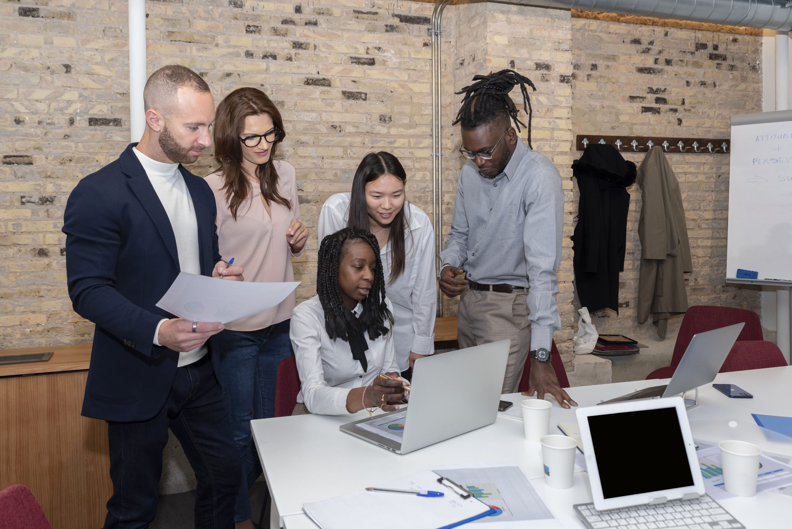 Young multi-ethnic business team working on a project, sharing ideas and analyzing national seo data around a colleague sitting at the table looking at the computer in an office
