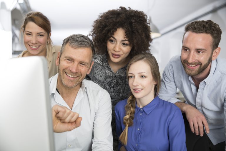 Smiling colleagues in office looking at monitor working on local SEO for a small business